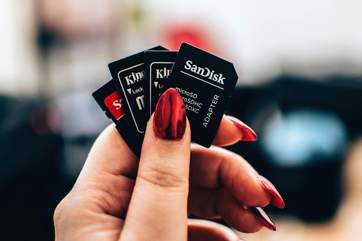 A hand with red painted nails holding several SD and microSD memory cards, including Sandisk and Kingston brands.